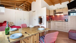Techo de madera, una mesa de comedor con platos y vasos, una cocina con armarios y estufa, y un sofá rojo.
