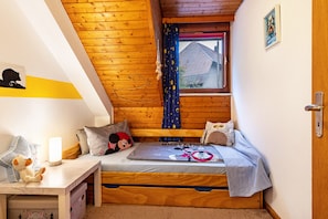 A cozy room with a wooden ceiling, a bed with Mickey Mouse bedding, a small desk with a lamp, and a window with curtains. - Ferienwohnung with 40qm (Dachsberg)