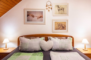 A bedroom with a wooden headboard, two bedside lamps, and three framed artworks on the wall. - Ferienwohnung with 40qm (Dachsberg)