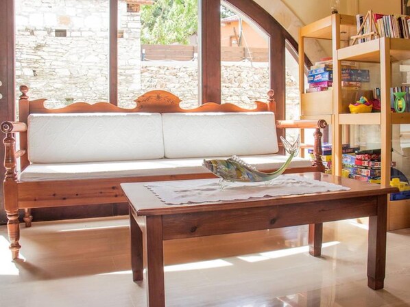 Un banco de madera con asiento acolchado, una mesa con un objeto de vidrio decorativo y una estantería con libros y juguetes.