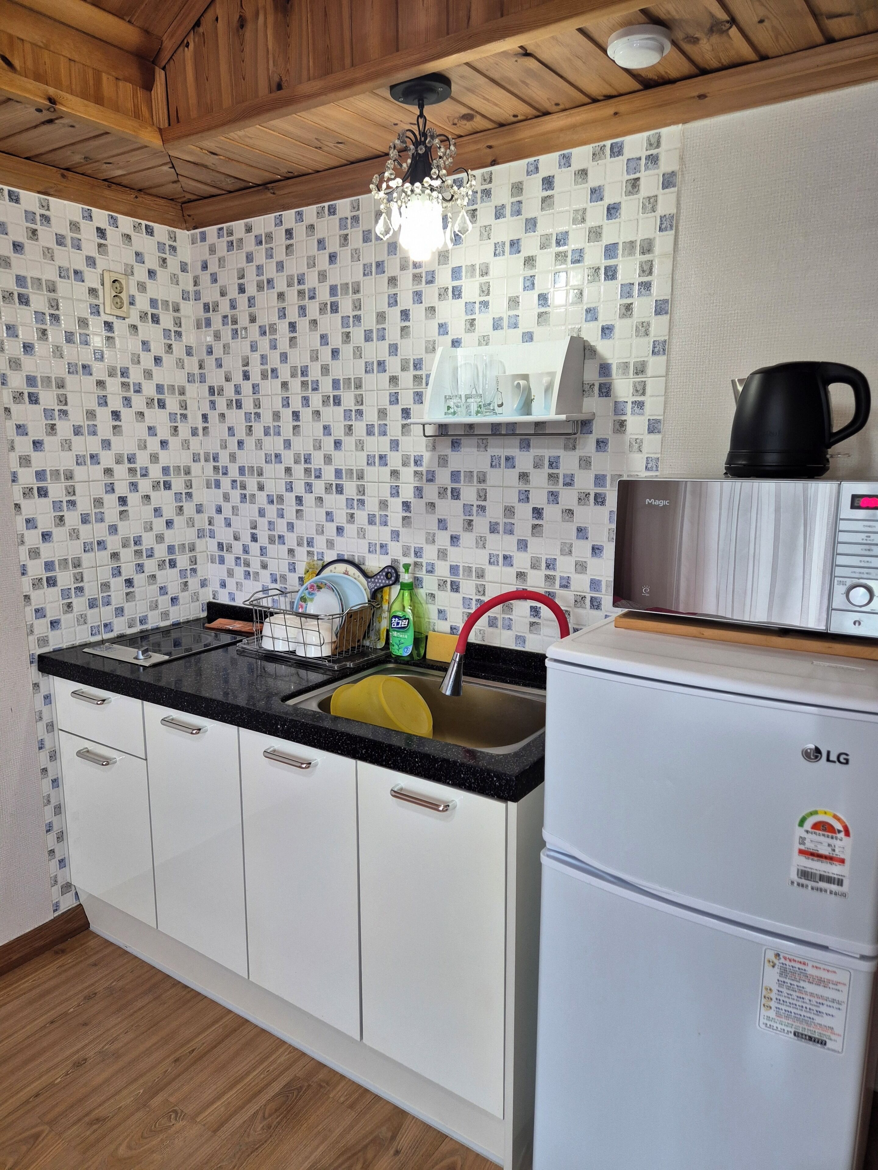 Eine Küche mit gefliestem Spritzschutz, einer schwarzen Arbeitsplatte, weißen Schränken, einer Edelstahl-Mikrowelle und einem weißen Kühlschrank.