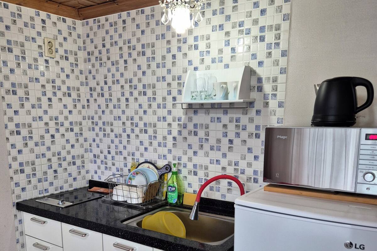 A kitchen with a tiled backsplash, a black countertop, white cabinets, a stainless steel microwave, and a white refrigerator.