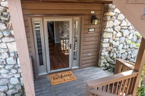 A wooden cabin entrance with a stone wall, a welcome mat, and a wooden deck. - Large Luxurious 3/3 Lake Home
 (Mount Ida)