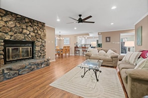A spacious living room with a stone fireplace, a ceiling fan, and a dining area in the background. - Large Luxurious 3/3 Lake Home
 (Mount Ida)