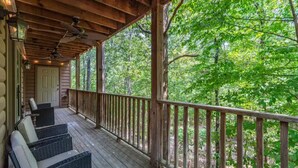 A wooden deck with wicker furniture, a wooden railing, and a view of a forest.