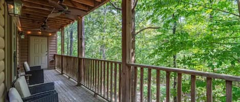 A wooden deck with wicker furniture, a wooden railing, and a view of a forest.