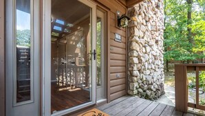 A wooden cabin entrance with a stone wall, a welcome mat, and a number sign indicating the cabin's location.