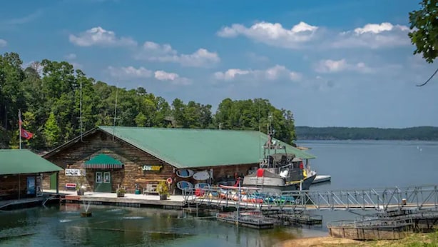A lakeside cabin with a dock, a boat, and a small building with a green roof.