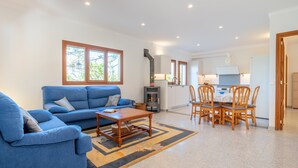 A living room with a blue sofa, a wooden coffee table, and a dining area with wooden chairs and a table. - Family-friendly villa with pool - Casa Mediterranea I (Cala Llombards)