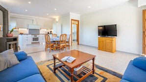 A modern living room with a sofa, coffee table, TV, and kitchen in the background. - Family-friendly villa with pool - Casa Mediterranea I (Cala Llombards)