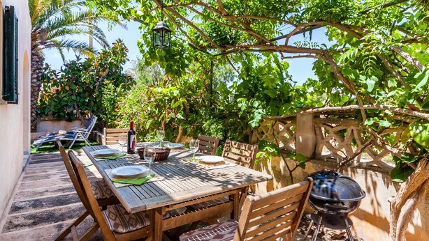 An outdoor dining area with a wooden table, chairs, and a barbecue grill. - Family-friendly villa with pool - Casa Mediterranea I (Cala Llombards)
