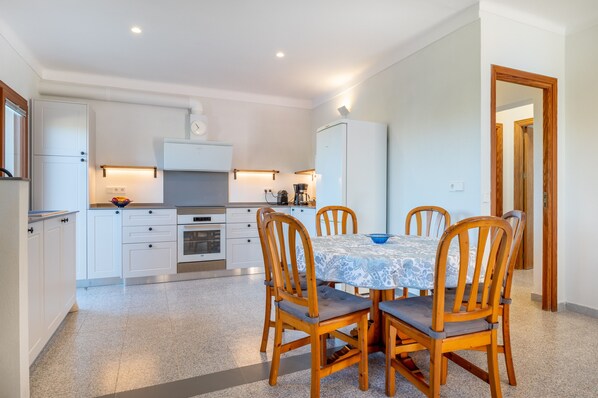 A modern kitchen with white cabinets, a dining table with four chairs, and a coffee machine. - Family-friendly villa with pool - Casa Mediterranea I (Cala Llombards)