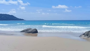 Ein Strand mit blauem Himmel, ruhiger Wellen und Felsen.