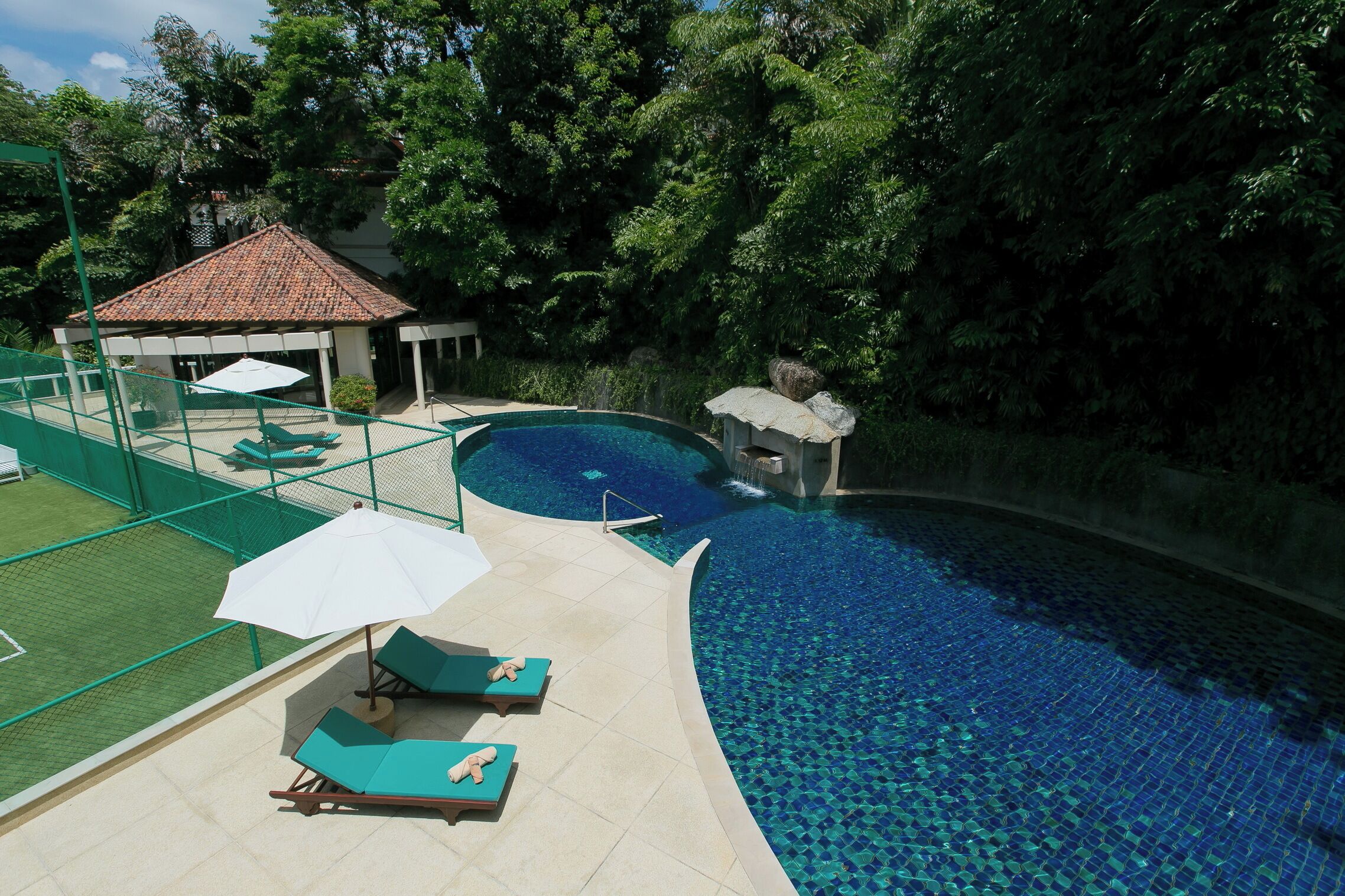 A swimming pool with a tiled edge, lounge chairs, and umbrellas.