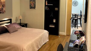A bedroom with a bed, a nightstand, a lamp, a bookshelf, and a desk with a vase of flowers. - Elegant Condo - European Charm (Palm Coast)