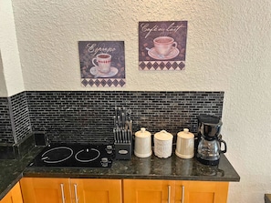 Una cocina con salpicadero de baldosas negras, estufa negra y armarios de madera. Hay dos dispensadores de café y una cafetera sobre la encimera.