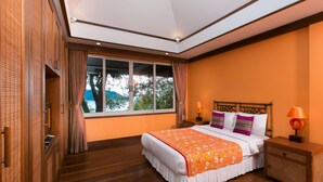 A bedroom with a large bed, wooden flooring, a view through a window, and a nightstand with a lamp. - Katamanda villa Sooksan Near Kata Noi Beach (Karon)