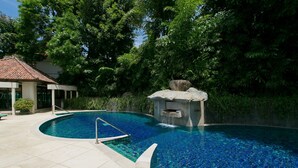 A swimming pool with a stone waterfall feature, surrounded by lush greenery and a tiled deck. - Katamanda villa Sooksan Near Kata Noi Beach (Karon)