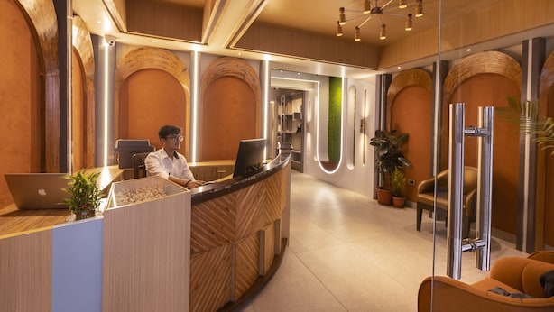 Un comptoir d’accueil avec un ordinateur portable, une personne assise derrière, et un intérieur moderne agrémenté d’éléments en bois et d’une cloison en verre.