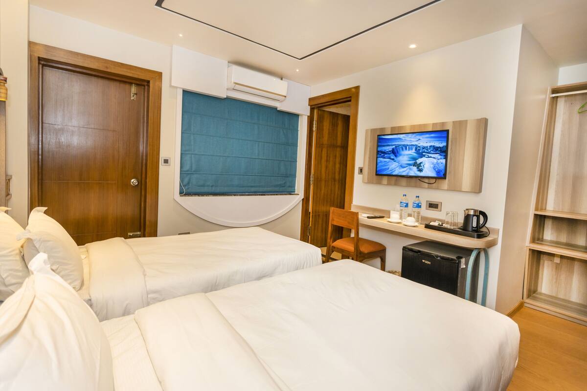 Ein Hotelzimmer mit zwei Betten, einem Schreibtisch, einem Fernseher und einer Minibar.
