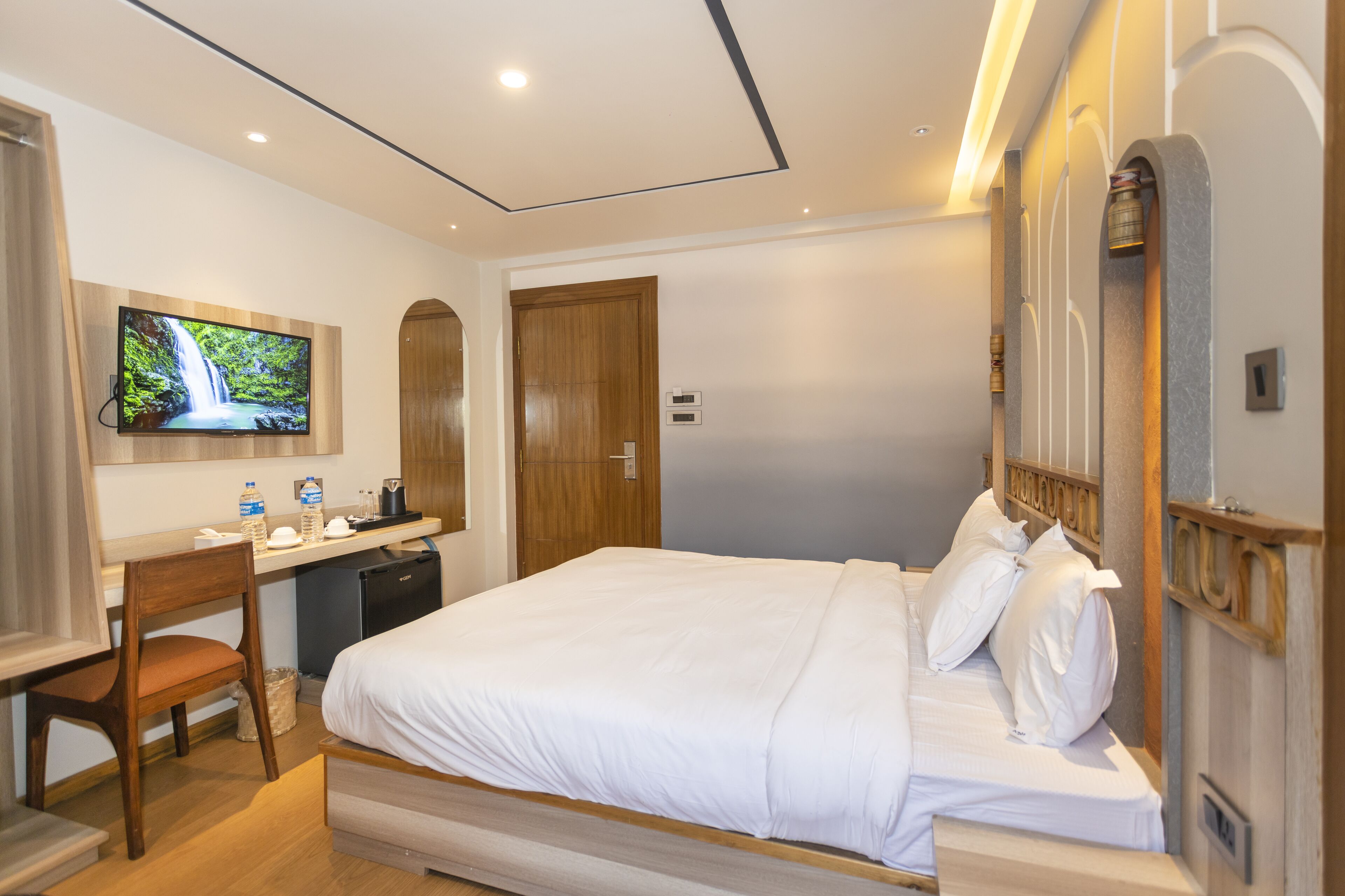 A hotel room with a bed, a desk with a chair, a television, and a wooden door.