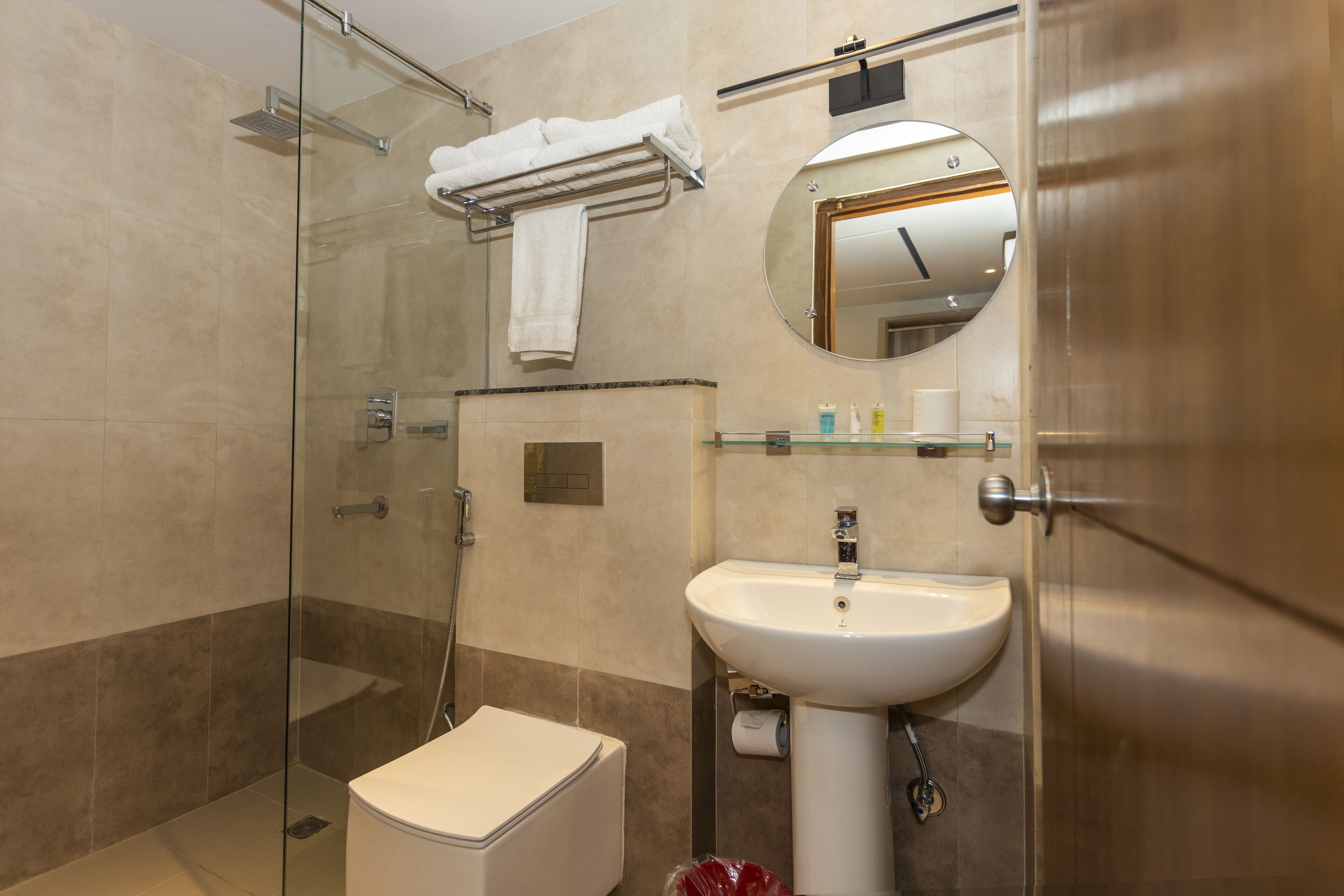 A modern bathroom with a glass shower enclosure, a white toilet, a sink with a mirror above it, and a towel rack with a white towel.