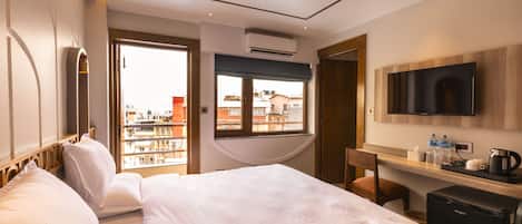 Habitación de hotel con una cama grande, un escritorio con cafetera, un televisor y vistas a edificios por la ventana.