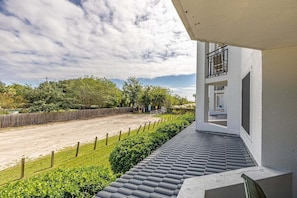 Uma varanda com vista para uma estrada e vegetação, um edifício branco com varanda e um céu claro.