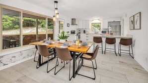Uma cozinha moderna com armários brancos, uma geladeira de aço inoxidável e uma área de jantar com mesa e cadeiras de madeira.