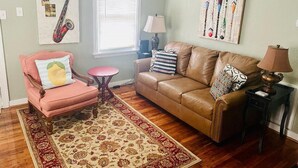 A living room with a brown leather sofa, a pink armchair, a small round table, a patterned rug, and wall art.