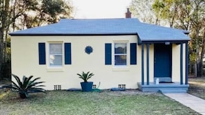 A single-story house with a gabled roof, a front porch, and a small front yard with a potted plant and a decorative wall piece.