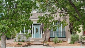Une maison à deux étages avec un porche à l’avant, une porte bleue et un petit jardin où poussent différentes espèces de plantes.