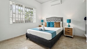 Une chambre à coucher avec un lit, deux tables de chevet, une fenêtre avec des barreaux et un appareil de climatisation.