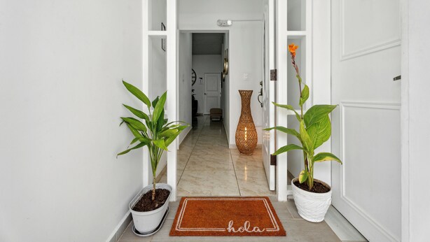 Un couloir aux murs blancs, doté d’un sol en marbre et orné de deux plantes en pot, une de chaque côté.