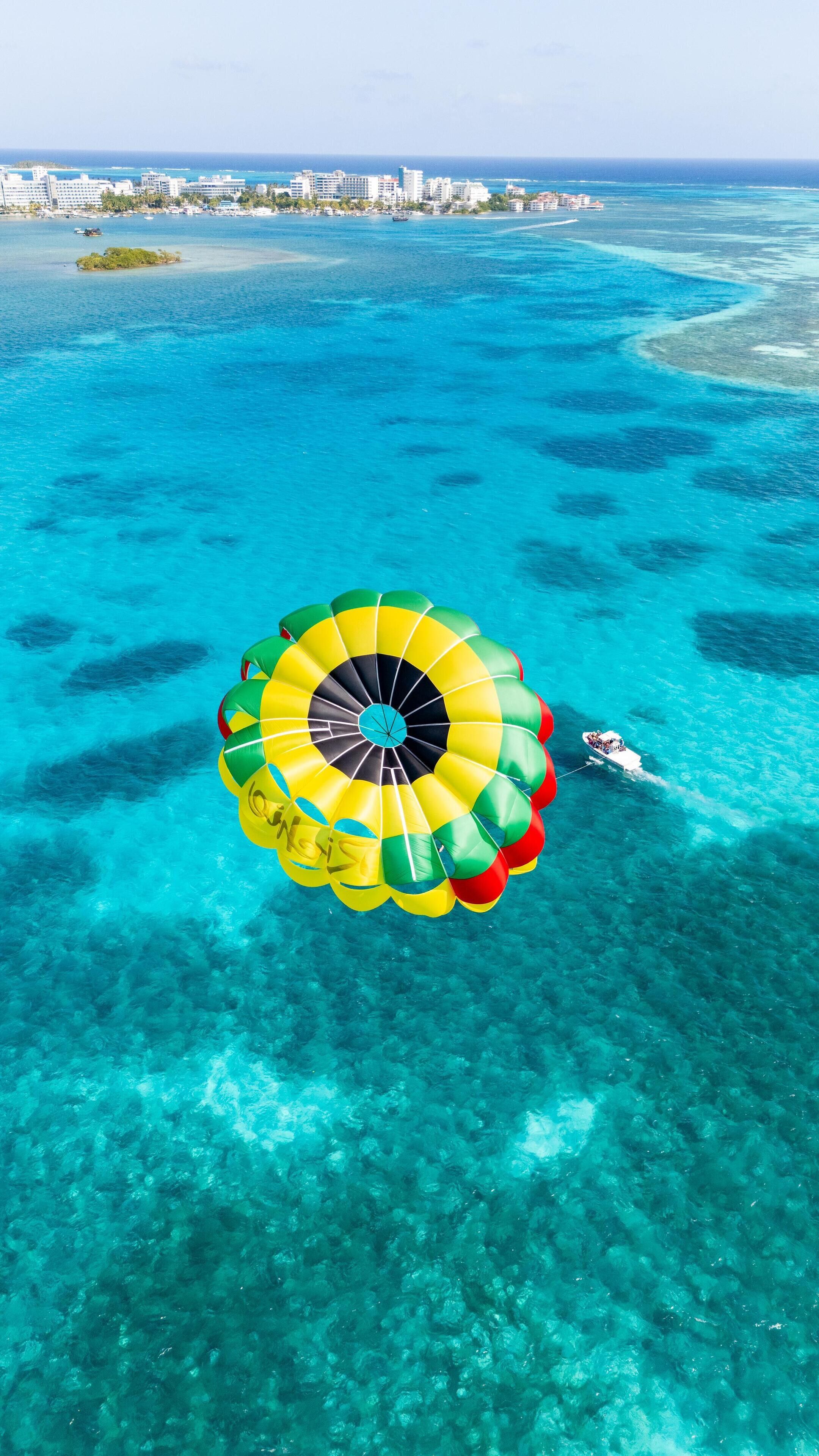 A parasail over clear turquoise waters with a distant cityscape.