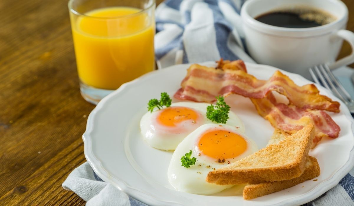 A plate with eggs, bacon, and toast, a glass of orange juice, and a cup of coffee on a wooden table.
