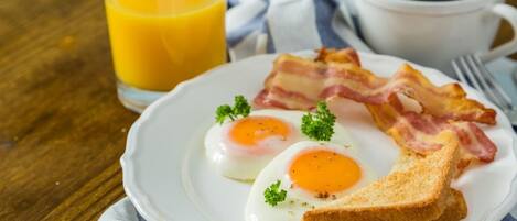 Un plato con huevos, tocino y tostadas, un vaso de zumo de naranja y una taza de café sobre una mesa de madera.