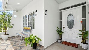Un hall d’entrée propre et moderne, avec un sol carrelé, un banc, des plantes en pot et une porte blanche dotée d’un panneau en verre.