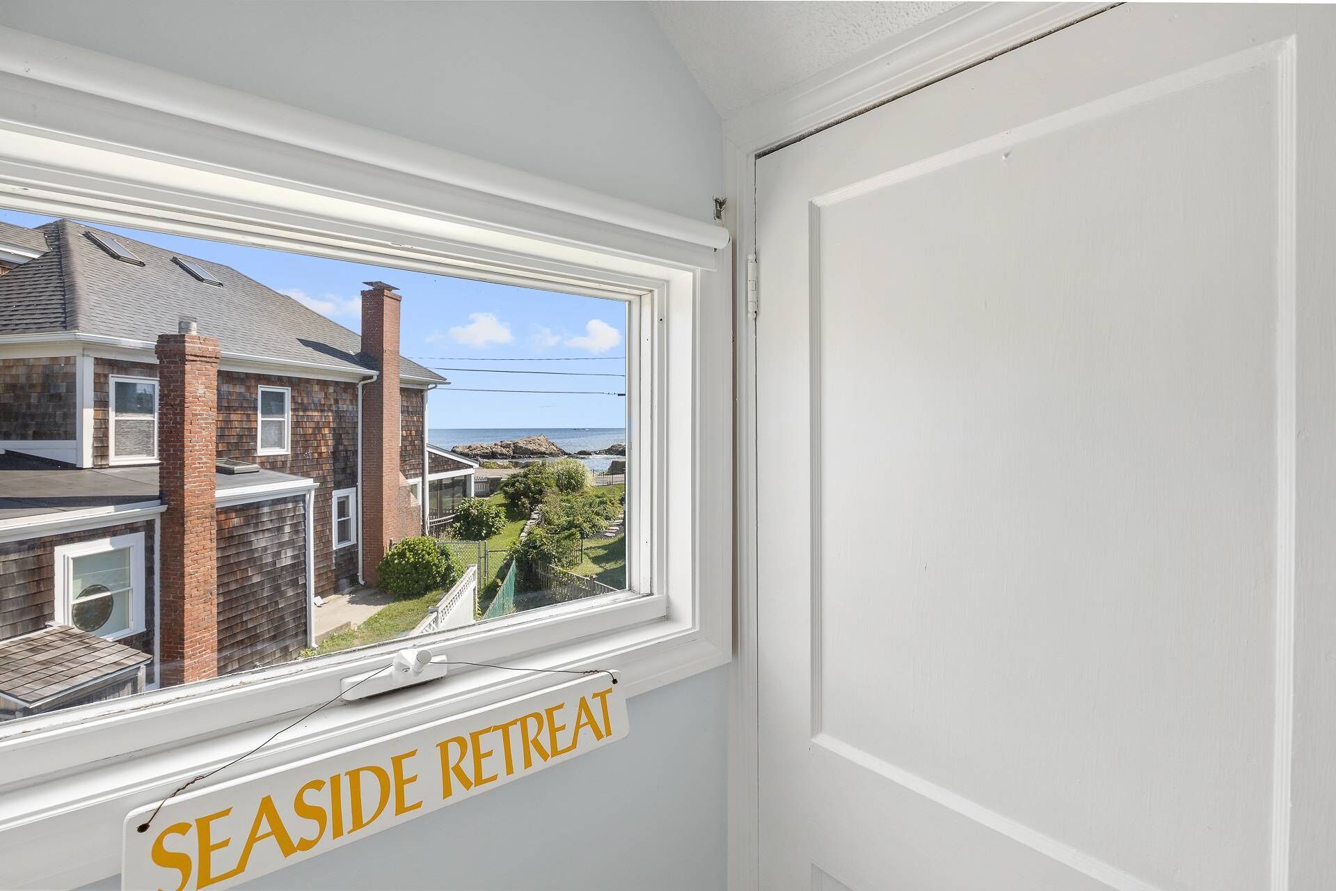 A window with a view of a coastal area, a brick chimney, and a sign that reads 'SEASIDE RETREAT'.