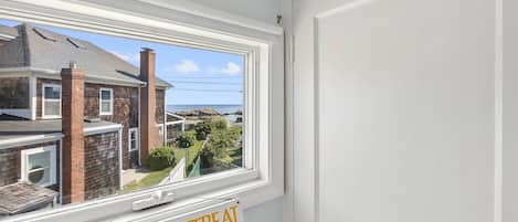 A window with a view of a coastal area, a brick chimney, and a sign that reads 'SEASIDE RETREAT'.
