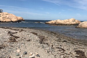 Ein felsiger Strand mit großen Steinen und einer kleinen Bausubstanz links.