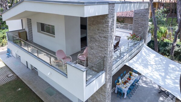 A modern two-story house with a balcony, a dining area, and a small garden. - La Villa in Pineta 10 Emma Villas (Castiglione della Pescaia)