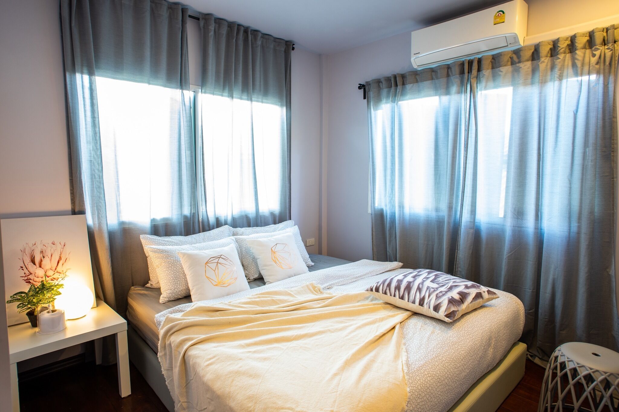 A neatly arranged bedroom with a bed, bedside table, and an air conditioning unit.
