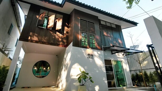 A modern two-story house with a balcony, a circular window, and a green door.