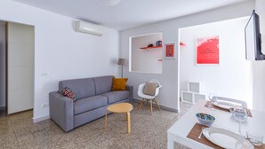 A modern living room with a grey sofa, a small round table, and a white dining table set for two. - Quite Shelter in Naples (Naples)