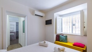 A hotel room with a bed, a window with white bars, a small TV, and a bathroom visible through an open door. - Quite Shelter in Naples (Naples)