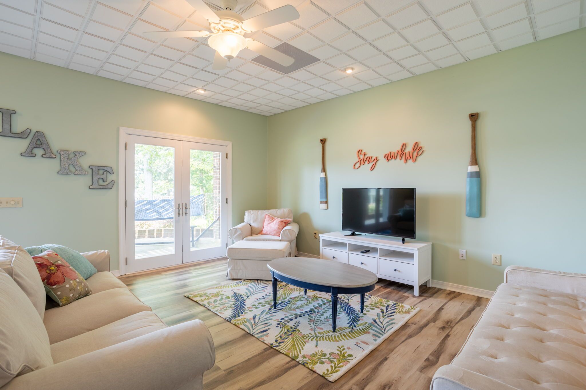 A living room with a television, a ceiling fan, and a large window.