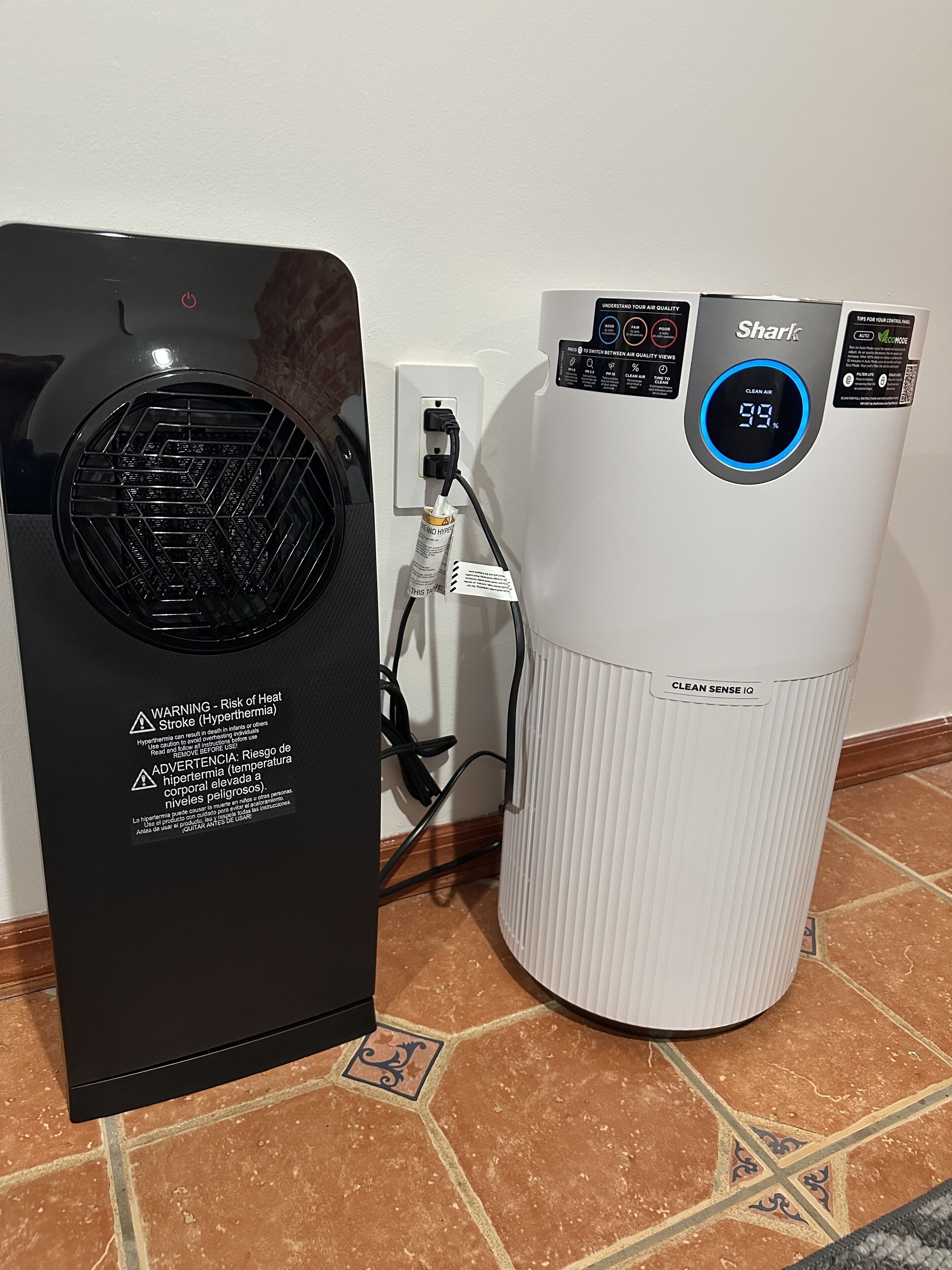 A black and a white air purifier with a digital display, connected to a power outlet.