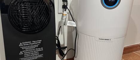A black and a white air purifier with a digital display, connected to a power outlet.