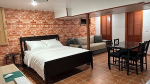 A room with a bed, a sofa, a dining table with chairs, and a small desk with a keyboard and mouse.